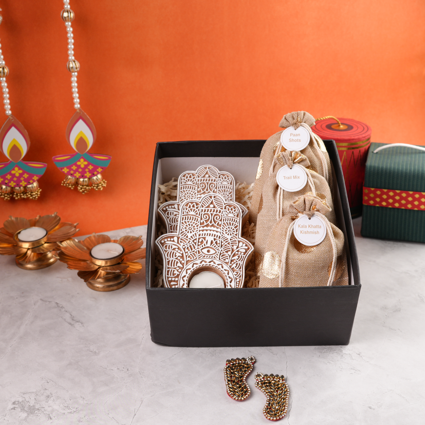 Open black Diwali hamper, top view showing layered hand-shaped tealight holders and golden-dot burlap pouches.