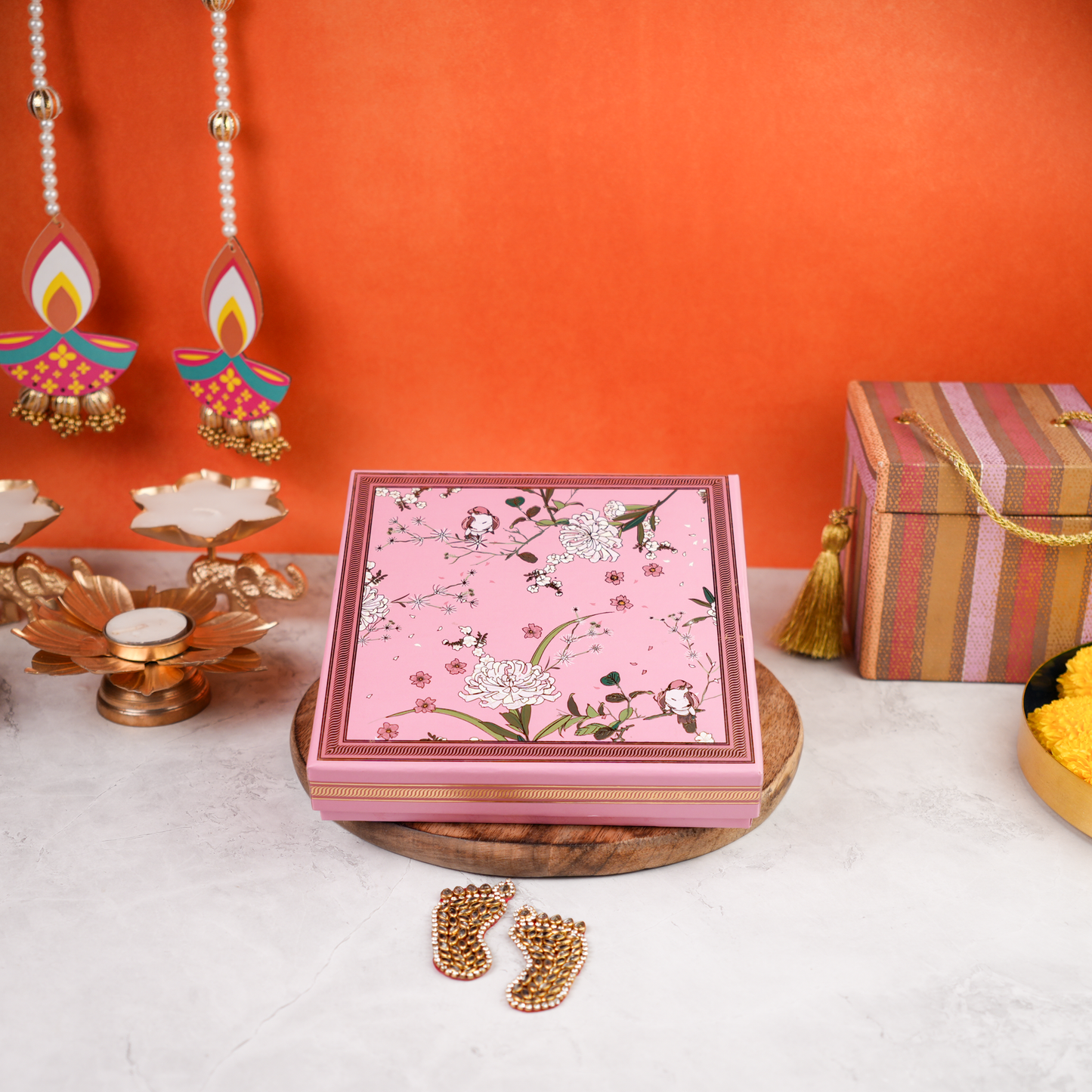 Wide front styled shot of the Floral Budget Diwali Gift Box closed, pink floral lid on a wooden platter with diyas and marigolds—an affordable option for corporate Diwali gifting.