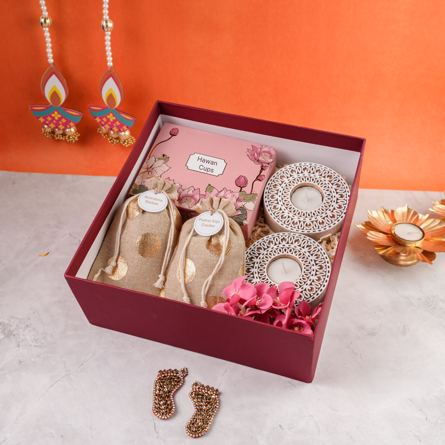 Open Garnet Glow Diwali Hamper showing hawan cups, festive potlis, and carved white tealight holders in maroon box.