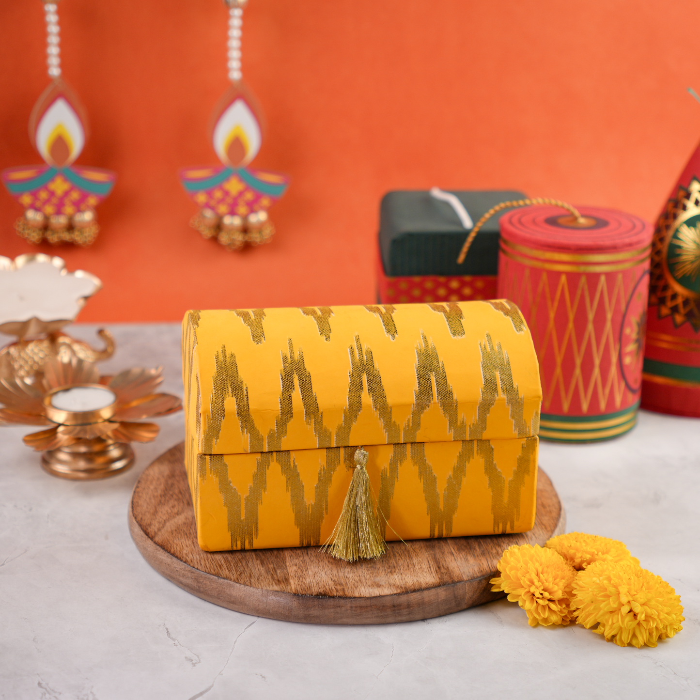 Ikat Diwali trunk hamper, saffron-and-gold dome lid with tassel, festive props in the background.