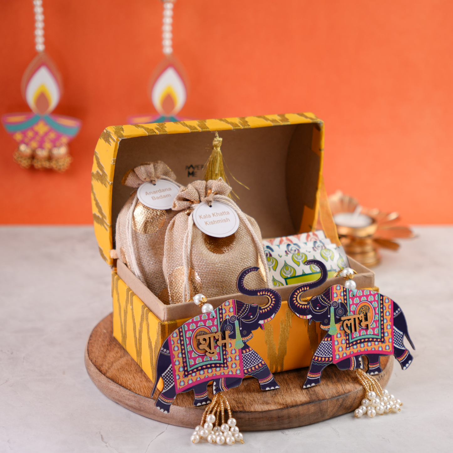 Open ikat trunk showing artisanal treats in jute potlis with Shubh–Labh elephant décor.