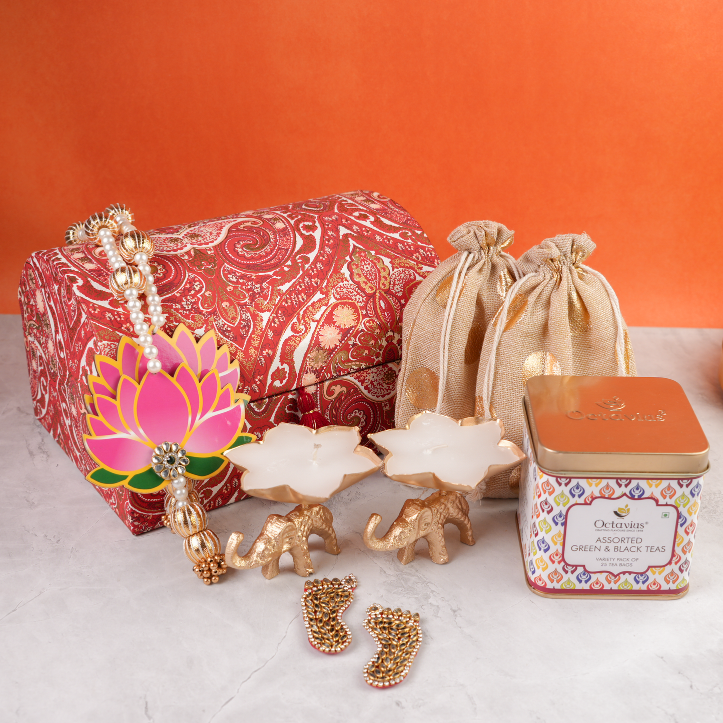 Angled closed view of Paisley Celebration Sandook Box featuring two golden potlis, Octavius tea tin, lotus-shaped candles, and decorative lotus dangler for festive gifting.