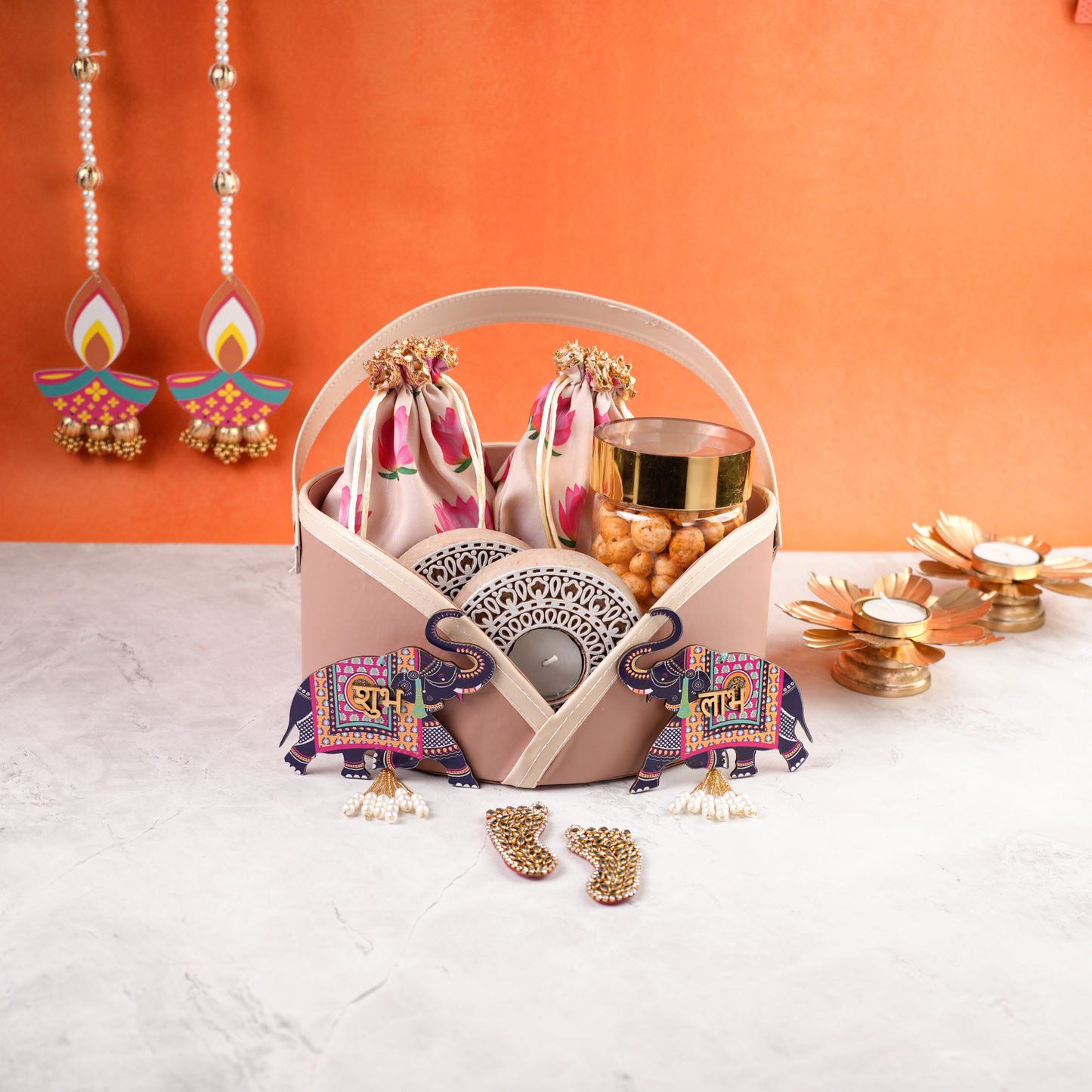 Elegant pastel pink Diwali hamper centered with decorative elephants, tealight candles, and dry snacks styled for festive gifting