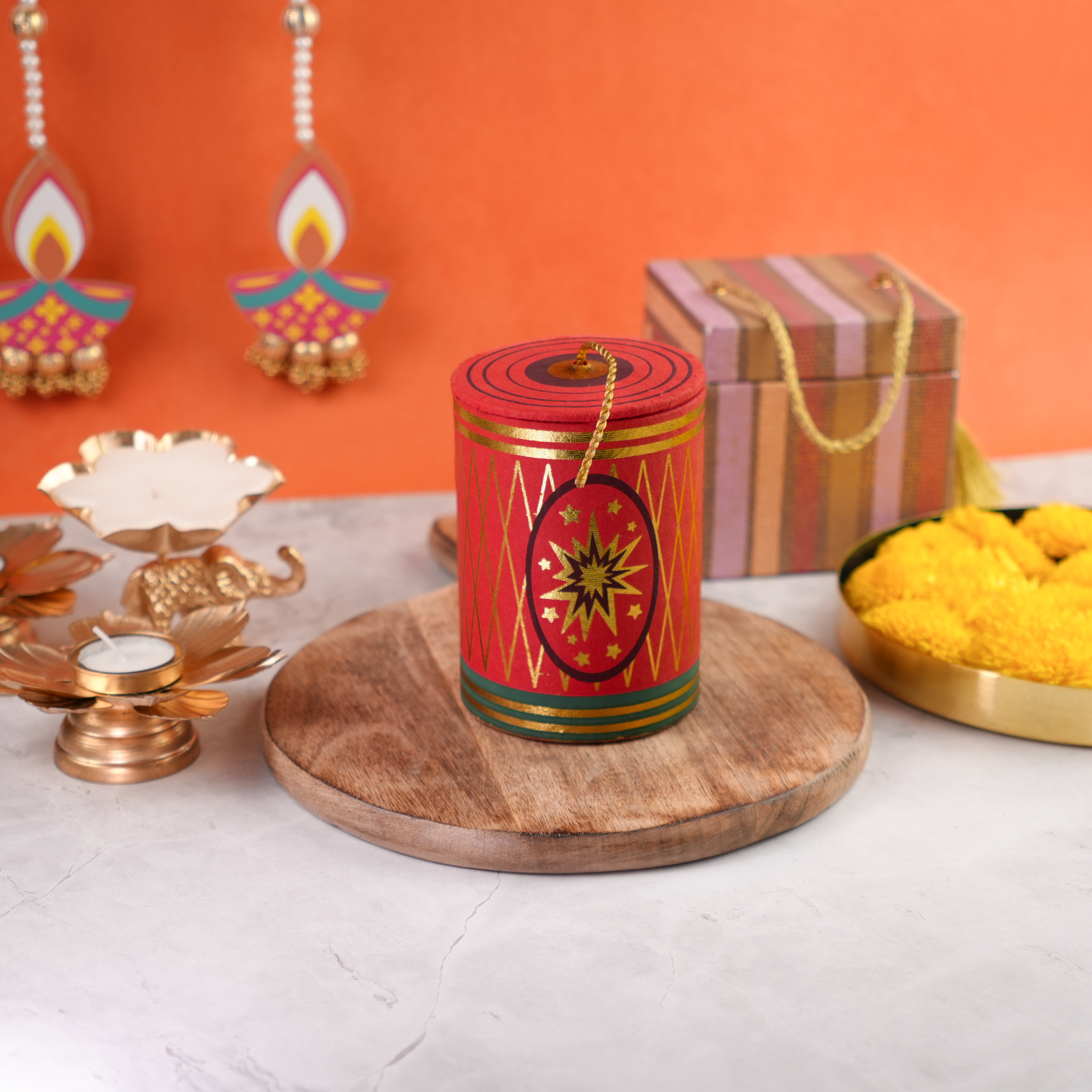 Red cracker-shaped Rangeela Chilly Bomb gift box placed on a wooden tray with festive decor and yellow marigolds in the background