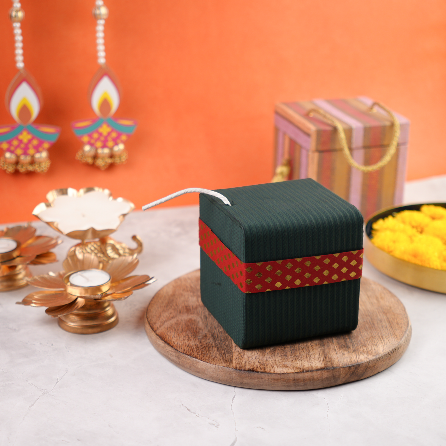 Angled view of green Diwali Sutli Dhamaka gift box with red festive band and cracker-style white fuse on top.