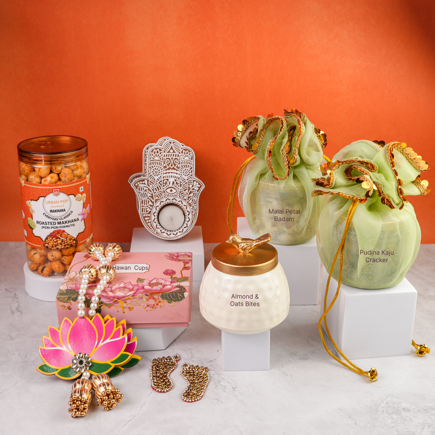 Detailed display of Wholesome Basket Diwali gift hamper products, including roasted makhana jar, ceramic candle jar, lotus pink chocolate box, festive potli bags, and carved tealight holder arranged with decorative accents.