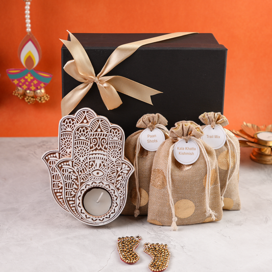 Closed black hamper with gold ribbon, hand-shaped carved tealight holder, three festive drawstring pouches and Laxmi Charan.