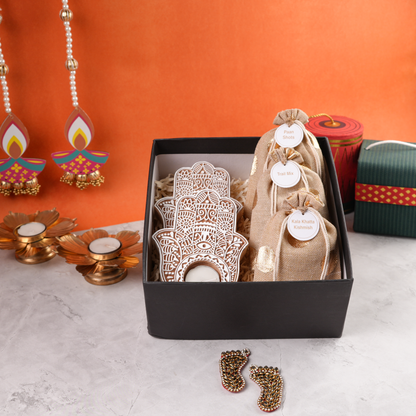 Open black Diwali hamper, top view showing layered hand-shaped tealight holders and golden-dot burlap pouches.