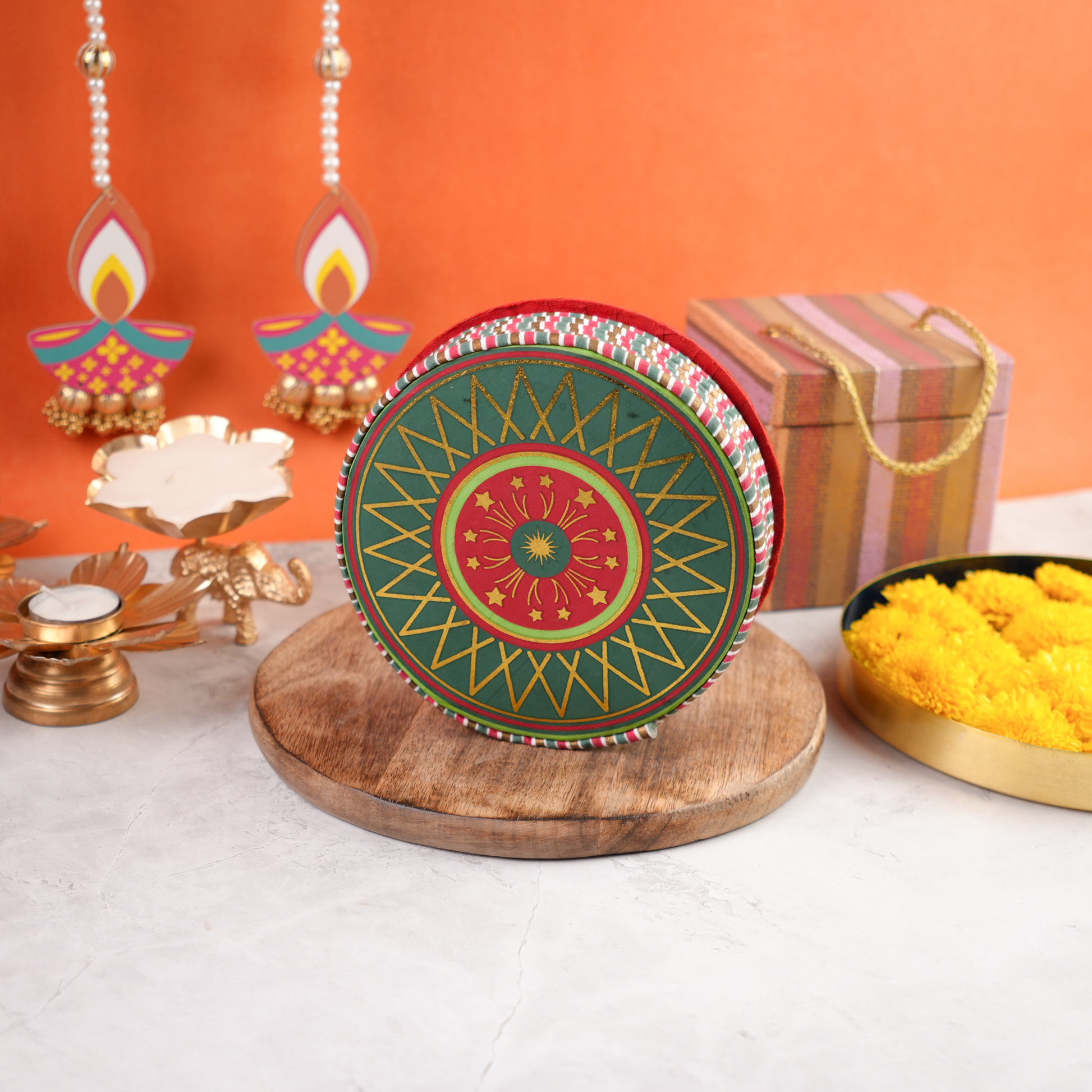 Chakri Diwali Gift Pack closed round cracker-shaped box in green and red festive artwork, placed on wooden base with Diwali décor.