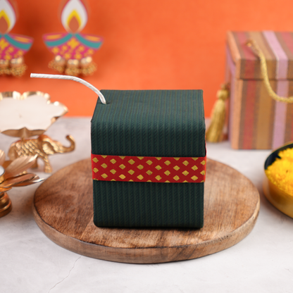 Closed green Sutli Dhamaka Diwali gift box with red festive band and white fuse, cracker-inspired keepsake design.