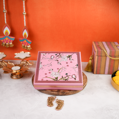 Wide front styled shot of the Floral Budget Diwali Gift Box closed, pink floral lid on a wooden platter with diyas and marigolds—an affordable option for corporate Diwali gifting.