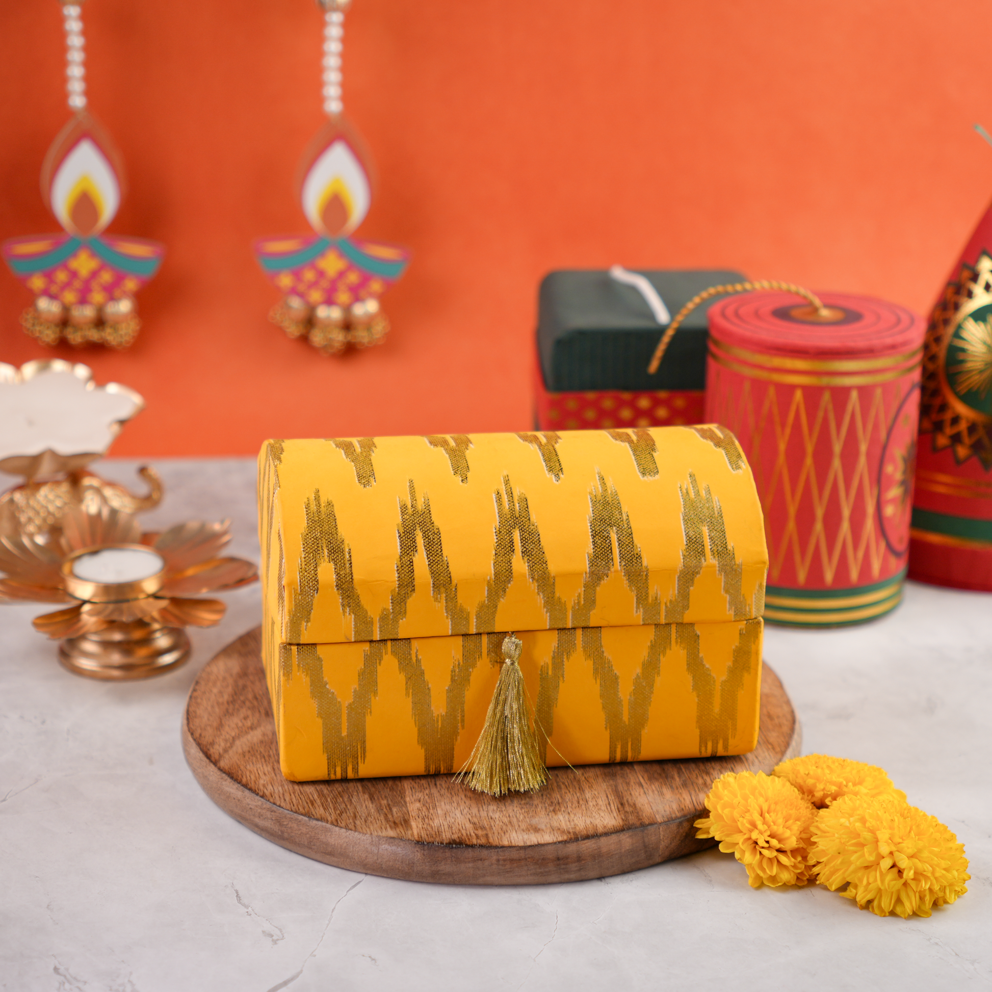 Ikat Diwali trunk hamper, saffron-and-gold dome lid with tassel, festive props in the background.
