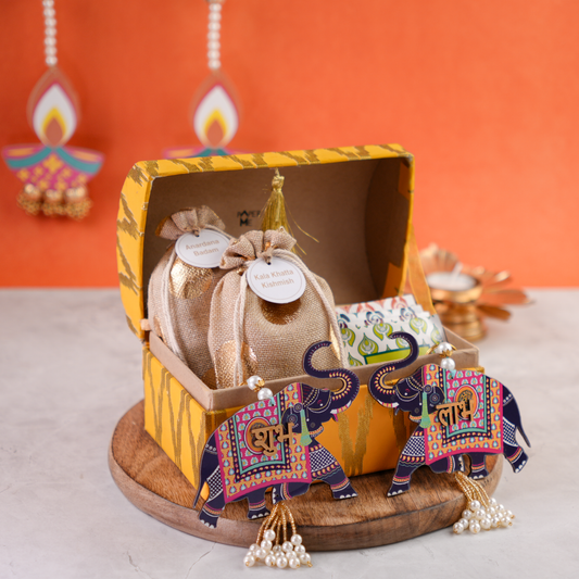 Open ikat trunk showing artisanal treats in jute potlis with Shubh–Labh elephant décor.