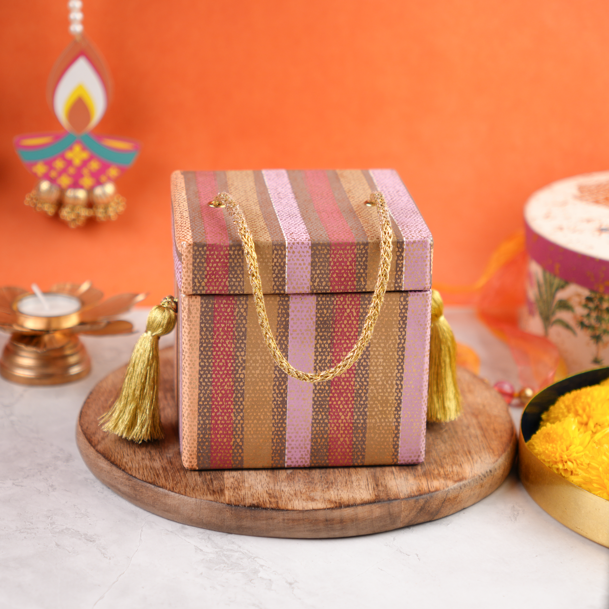 A closed striped gift box with gold tassel handles, trunk-style design, photographed on a wooden base against beautiful backdrop.