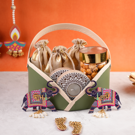 Pastel green Diwali gift basket with festive elephants, tealight holder, golden pouches, and snacks against orange backdrop