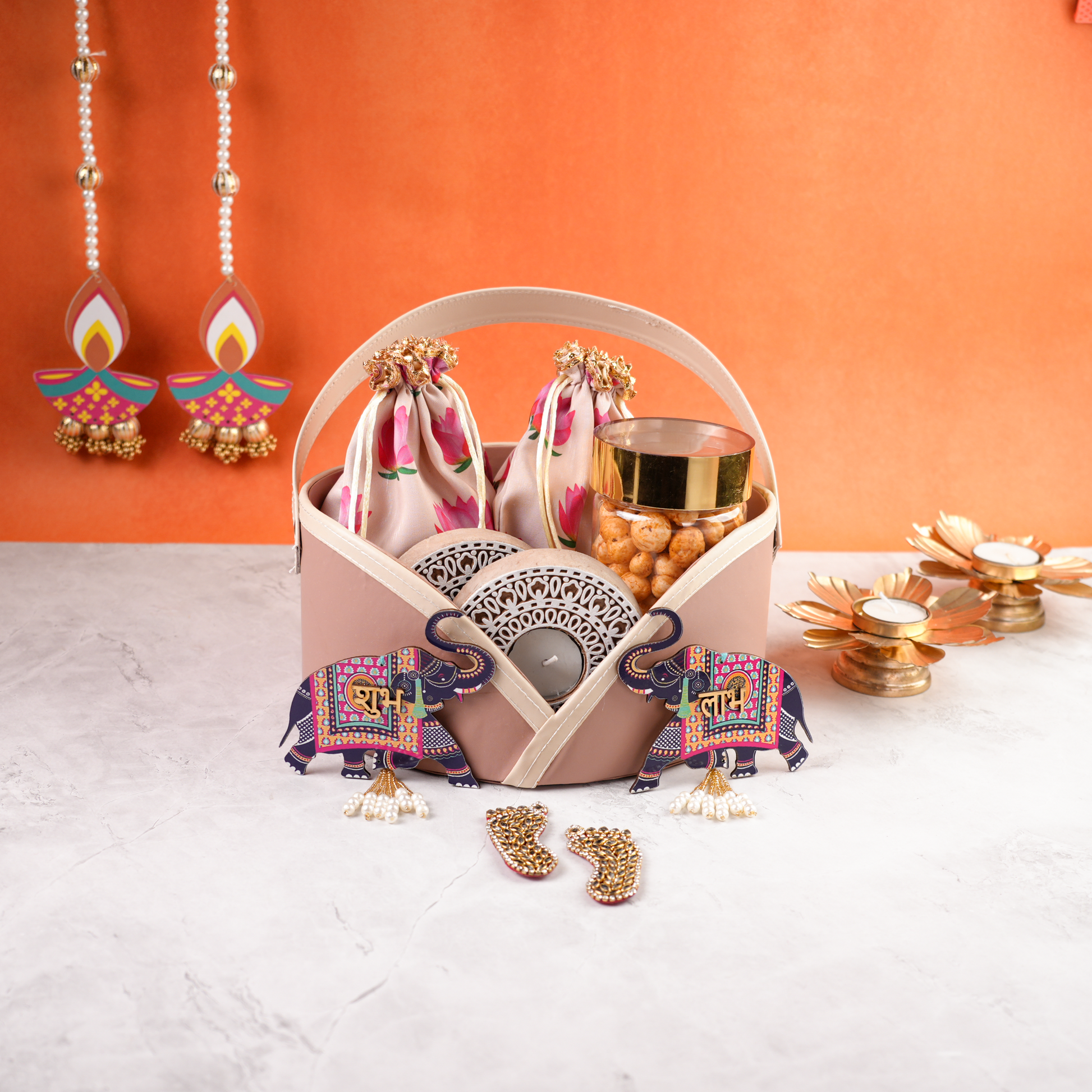 Elegant pastel pink Diwali hamper centered with decorative elephants, tealight candles, and dry snacks styled for festive gifting