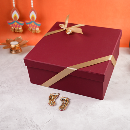 Closed Ruby Royale Diwali Hamper maroon gift box with golden ribbon, festive background and laxmi charan.